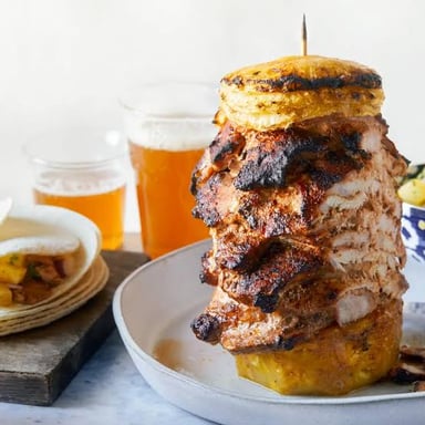 Al pastor pork being shaved from a vertical spit onto tacos.