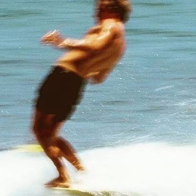 A surfer near the nose of a longboard, with toes extending over the front edge.