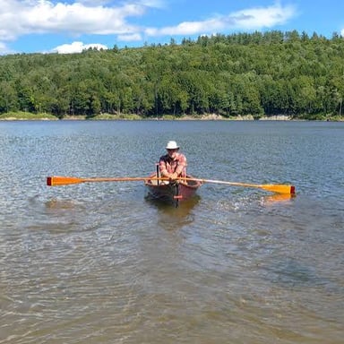 A person using oars to move a small boat across a lake.