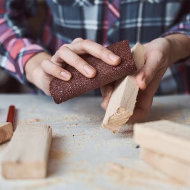Sandpaper rubbing and wearing down a wooden surface.
