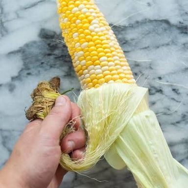 Hands peeling the husk away from an ear of corn.