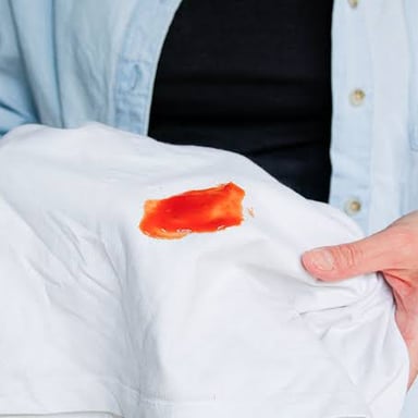 A person applies stain remover to a shirt before washing it.