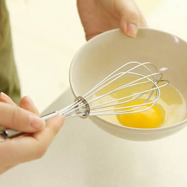 Eggs being beaten in a bowl with a wire whisk.