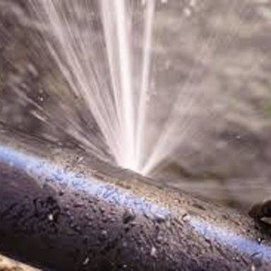 A ruptured pipe spraying water from a split opening.