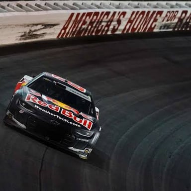 Stock cars racing around the banked curve of an oval racetrack.