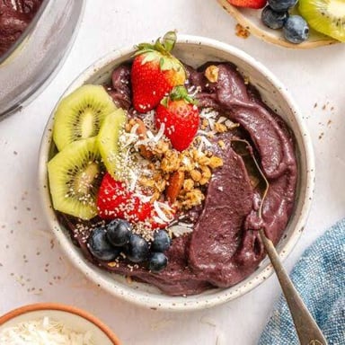 Dark-purple açaí berries beside a bowl of açaí purée topped with fruit.