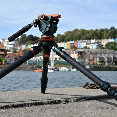A camera tripod with three legs spread out beneath its central mount.