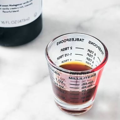 A measuring cup containing a small quantity of sugar.