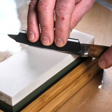 A craftsperson draws a blade along a honing stone to sharpen its edge.