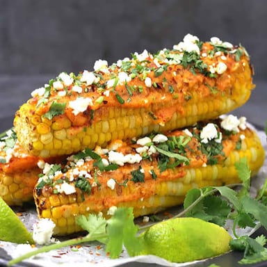 Grilled Mexican corn on the cob topped with creamy sauce, cheese, chile, and lime.