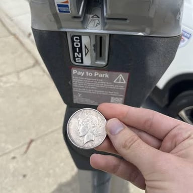 A hand putting coins into a parking meter.