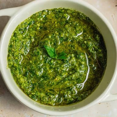 Green basil pesto served in a bowl, with fresh basil nearby.