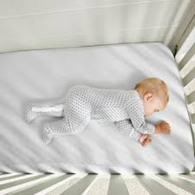 Baby sleeping in a crib covered by a fitted crib sheet