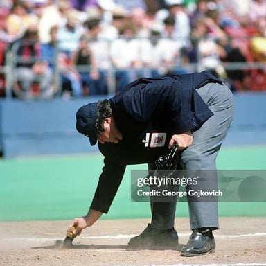 A baseball umpire brushing dirt from home plate.