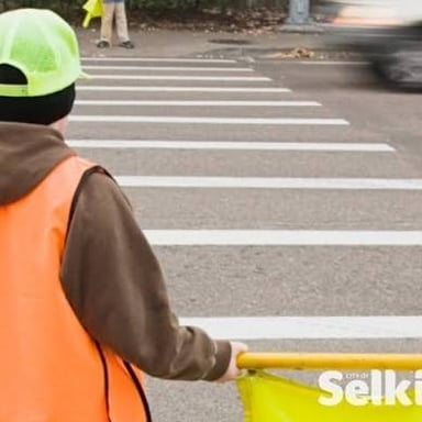 A crossing guard wearing a bright safety vest beside a crosswalk.