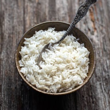 A bowl of cooked rice with rice plants in the background.