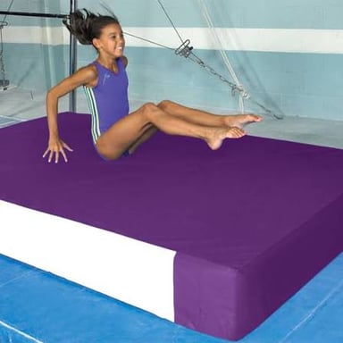 A gymnast landing on a padded mat in a gym.