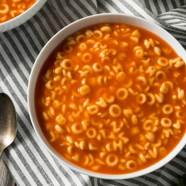 A bowl of soup containing small alphabet-shaped pasta.