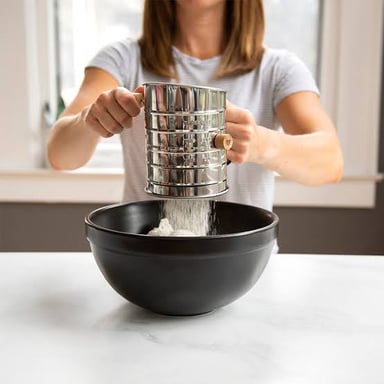 A handheld kitchen sieve being used to sift flour.