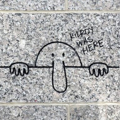The familiar Kilroy doodle, with a long-nosed figure peeking over a wall beside the words “Kilroy was here.”