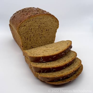 A sliced loaf of rye bread with caraway seeds visible in the crumb.