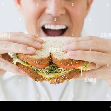A person taking a large bite of a sandwich.