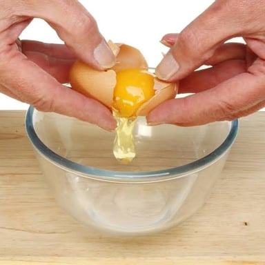 An egg being added to cake batter in a bowl.