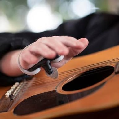 A hand brushes across the strings of an acoustic guitar.