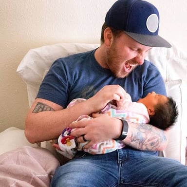 A parent holding a newborn, illustrating the sense of fathering offspring.