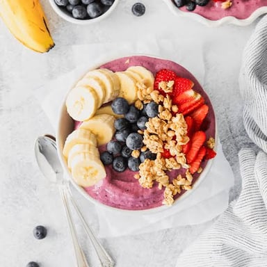 Dark açaí palm fruit beside a breakfast bowl topped with fruit and granola.
