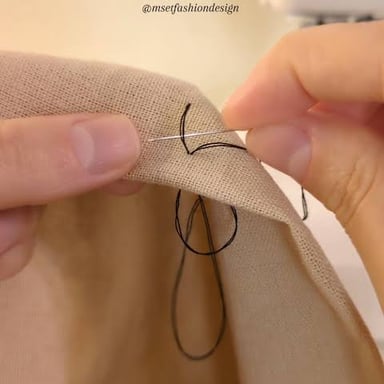 A person stitching a seam in fabric with a needle and thread.