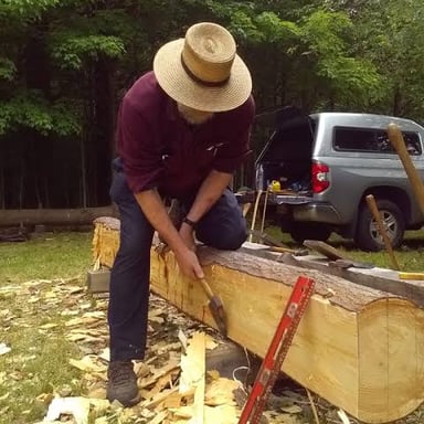 An axe being used to cut and shape a piece of wood.