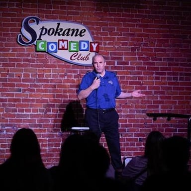 A comedian holding a microphone onstage before an audience.