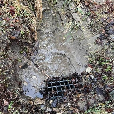 A drain blocked by debris and unable to carry water freely.