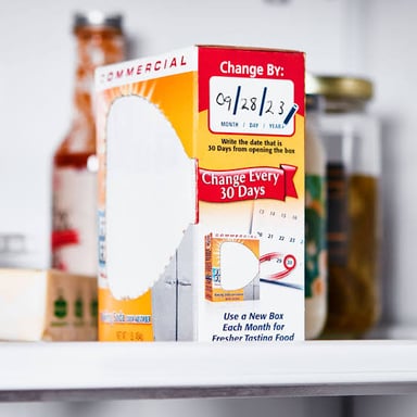 An open refrigerator with a box of baking soda used for odor control.
