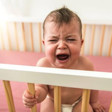 An infant resting in a crib, illustrating the soft sound called a coo.